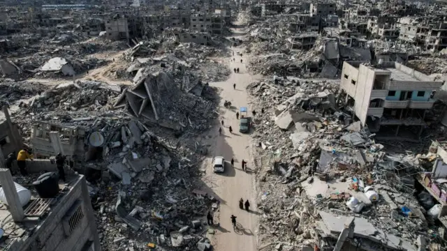 Palestinians walking along a street among the rubble of destroyed buildings