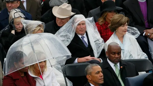 George Bush sitting down, with a plastic rain poncho draped over his head