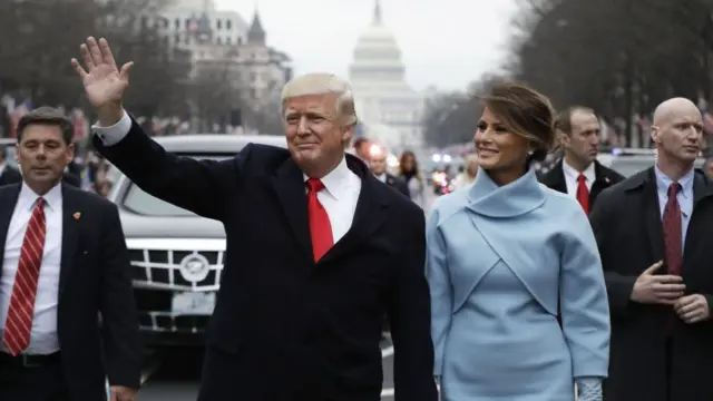 Trump waves to the crowd while holding the hand of his wife, Melania. The Capitol building is visible in the background