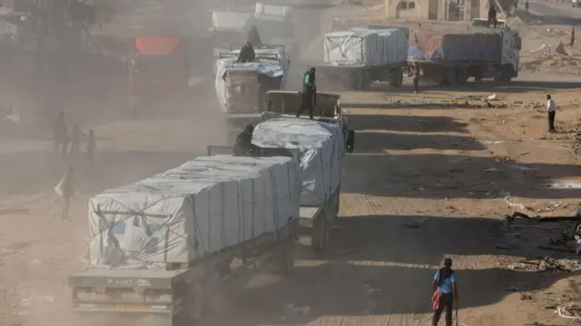 Humanitarian aid trucks enter Gaza after the ceasefire. On top of one of the lorries is an armed mad in a green jumper, bullet proof vest and gun