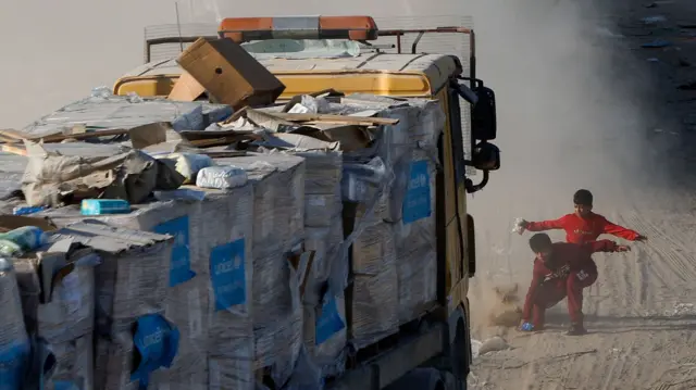 Children rush to pick up aid which has fallen onto the road in front of a moving truck