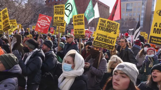 A large group of people wearing jackets, scarves and hats hold signs reading: 'The people will defeat Trump's extreme-right agenda!' Party for Socialism and Liberation