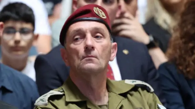 Israel chief of staff halevi sitting down in military fatigues and red beret with military broach. Several people sitting behind him, blurred