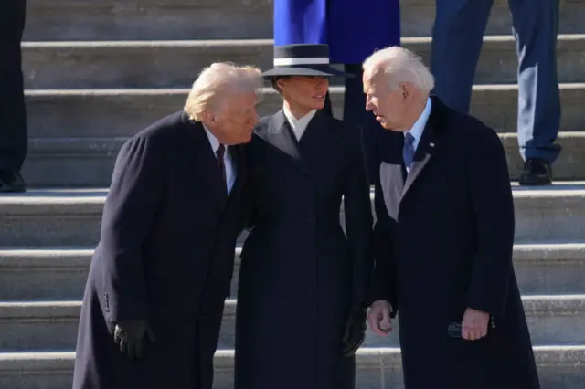 Trump, Melania Trump and Biden huddled together on some grey steps