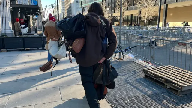 Back of a person holding about a dozen women's handbags