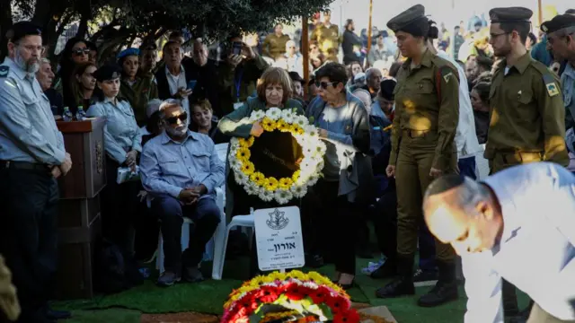 Mourners attending a funeral whilst holding flowers at the grave