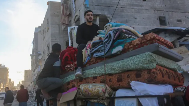 A male sits on top of several mattresses and blankets.