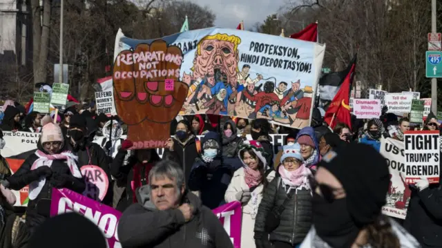 Front view of a crowd of protesters holding signs opposing Trump