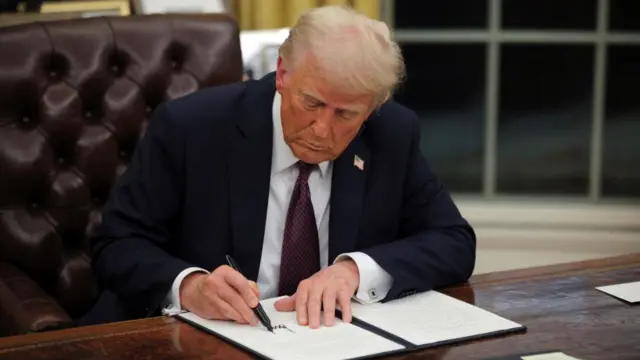 Trump signs an executive actions in the Oval Office, he holds a large black pen to a document in a black folder