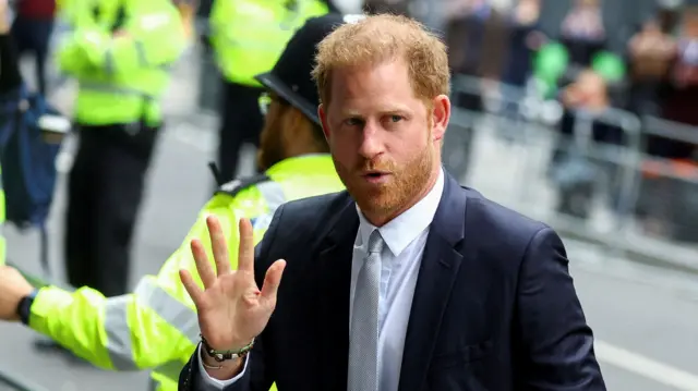 Prince Harry waves, with police in the background.