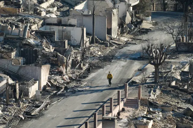 A man walks down a street of damaged houses burnt from the fire