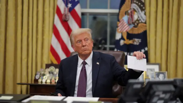 Donald Trump sits at his desk and holds up an envelope