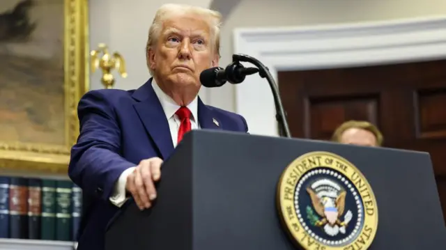 Taken from below looking upwards, Trump leans on the presidential lectern, looking stern