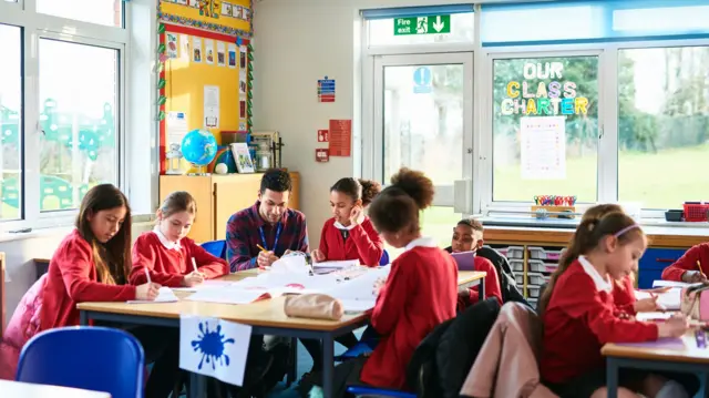 Children and a teacher speak in a classroom - file image