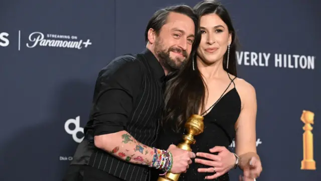 Kieran Culkin holding an award whilst embracing his wife at the Golden Globe awards