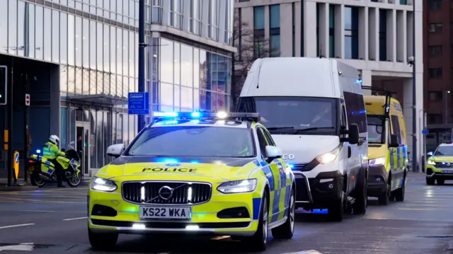 A white van drives between a marked police car and a marked police van