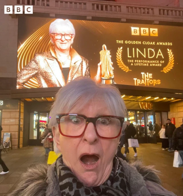 Linda looking shocked in front of the billboard in central London