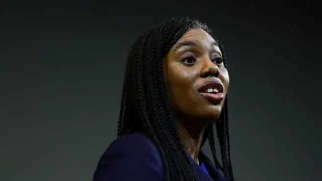 Kemi Badenoch close up during speech. She's wearing a blue top and her hair down as she looks to her right