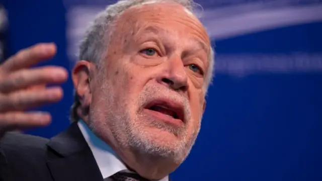 Robert Reich, former US labour secretary under the Clinton administration, shot from shoulders up, gesturing with hand gesturing and blue blurred background