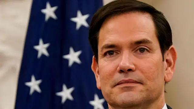 US Secretary of State Marco Rubio stands in front of an American flag