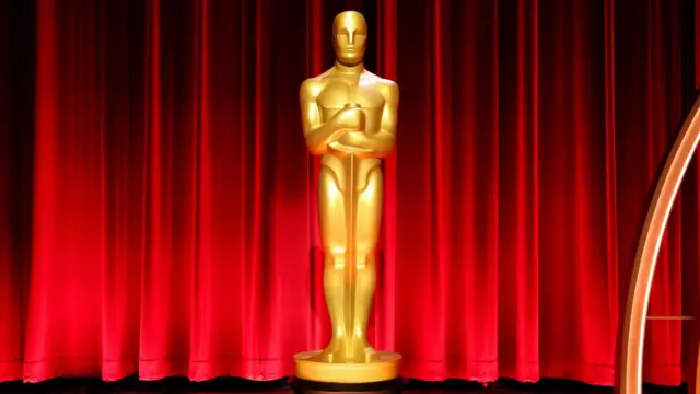 A golden Oscar trophy is pictured in front of a red curtain