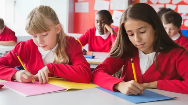 school girls are sitting in a classroom wearing red cardigans