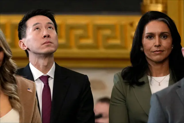 Shou Chew in dark suit and red tie looks at ceiling while Tulsi Gabbard stares straight ahead in olive blazer and white T-shirt