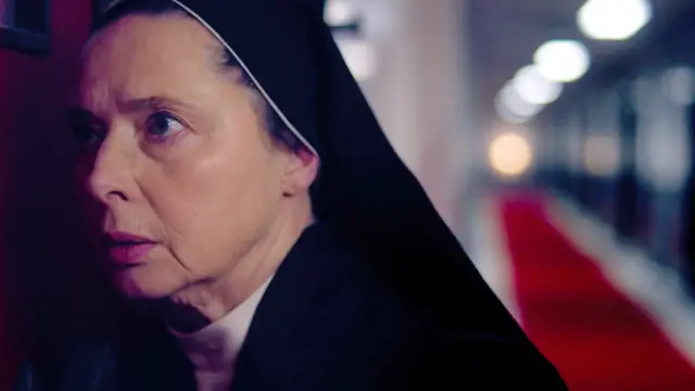 Isabella Rossellini dressed as a nun leaning into a door as she listens in Conclave