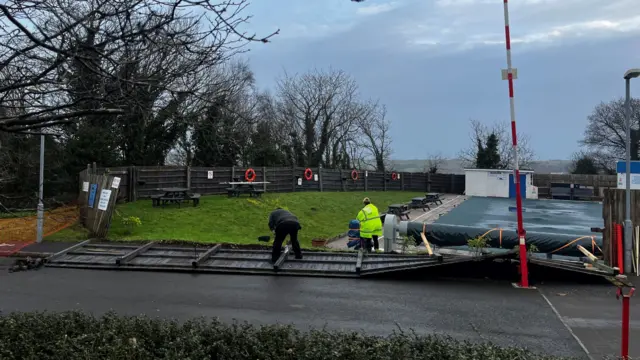 A picture of Dartmouth Outdoor Pool. Workers are clearing up the area and fixing the fence