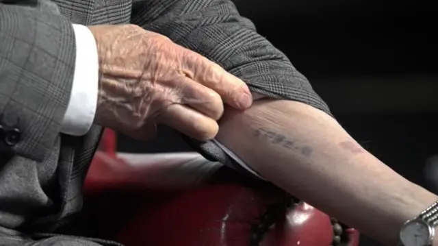 Arek Hersh shows his black ink Auschwitz tattoo reading B7608 on his left forearm as he pulls up his jacket and shirt sleeves