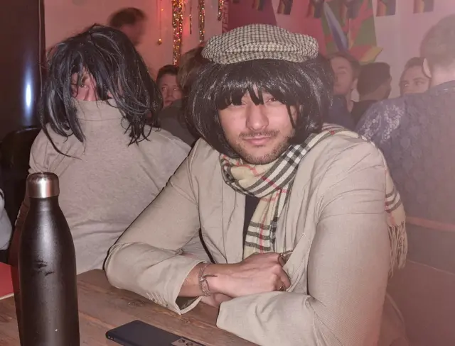 Two people in a pub dressed up as Claudia Winkleman with black wigs on