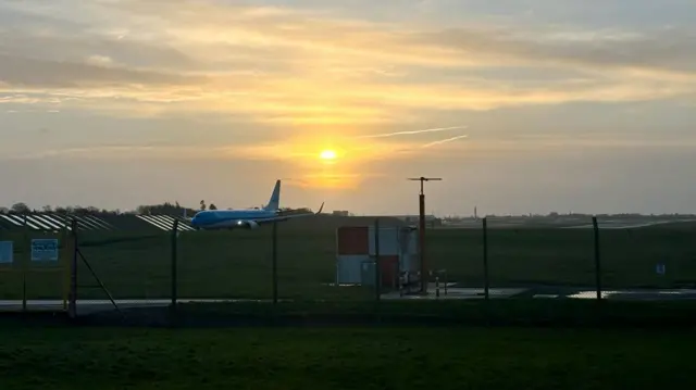 An airfield with the sun rising and an airplane on the runway