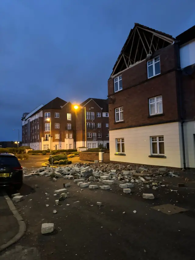 A house missing the side wall of it's attack with debris lying across the road