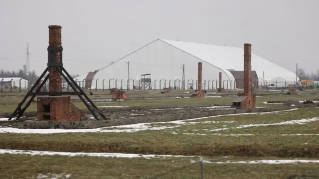 White tent erected on the grounds of Auschwitz-Birkenau to host the commemorations. The remains of barracks, mostly red-brick chimneys, stand in a field of grass