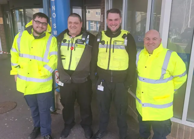 Maintenance assistant Luke Ferguson, security team members Gary Pickard and Aaron Sparrow, and plumber Ste Loughran smiling outside the University Hospital of North Tees. They are wearing high visibility clothing.