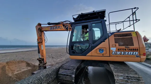 Andrew Walker is in a yellow tractor and digging sand at the beach