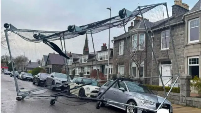 Large netted frame on wheels on top of cars on a road.