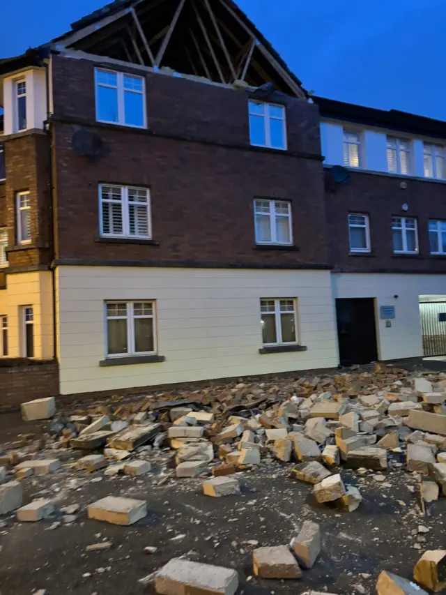 A house missing the side wall of it's attack with debris lying across the road