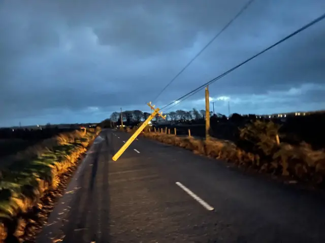 A telegraph pole still attached to wires but hanging in the middle of a road