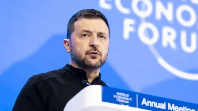 Volodymyr Zelensky addresses World Economic Forum in Davos from behind a lectern. He's standing, wearing a black shirt