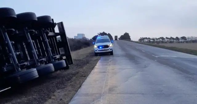 A lorry is overturned with a police car  in attendance