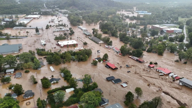 Aerial view of Asheville, North Carolina in the aftermath of Hurricane Helene in September. Buildings and cars are submerged under brown water as flooding spread