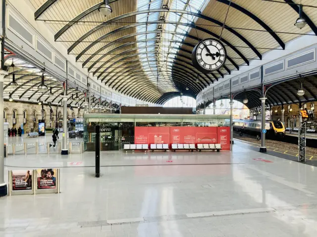 Empty concourse at Newcastle train station. Only one train is visible. One person is heading into a coffee shop.