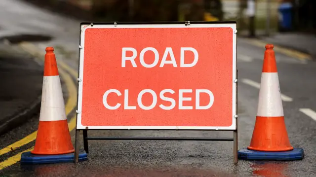 A "road closed" sign with two traffic cones on either side of it