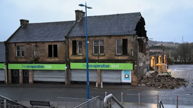 A side of a Coop supermarket building is exposed, brick and rubble on the pavement