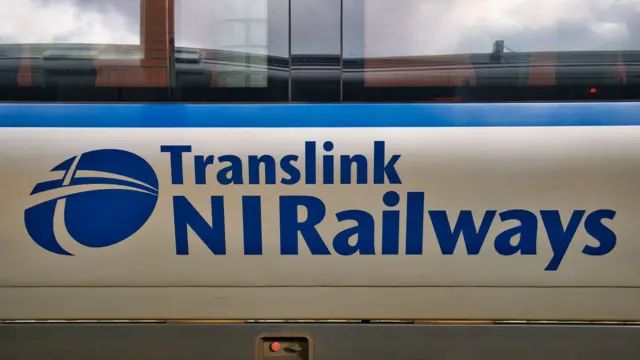 Side of a silver and white train with the logo of "Translink NI Railways" printed on it.