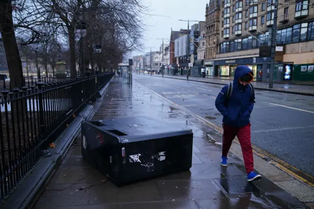 A person walks by an upturned bin on Princes Street in Edinburgh during Storm Eowyn