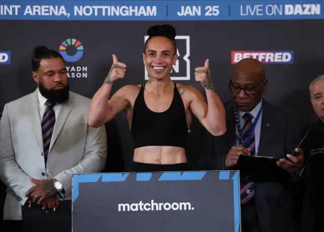 Mea Motu smiling with her thumbs up on the scales