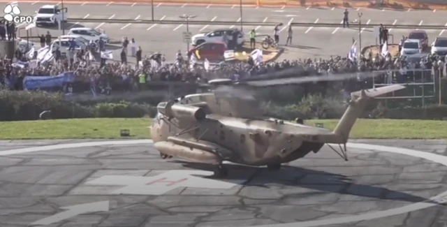 Helicopter lands on helipad with crowd on people in background