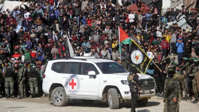 A vehicle of the International Committee of the Red Cross (ICRC) drives in front of Palestinians and Hamas militants gathered in the center of Gaza City